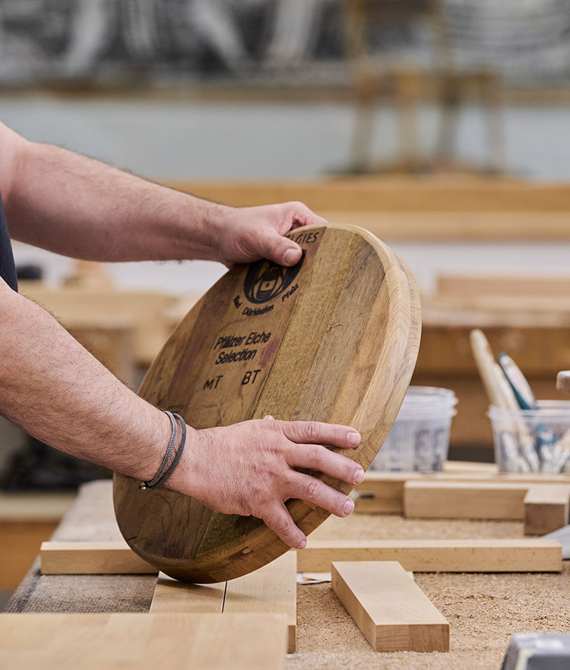 Handwerker hält ein rundes Holzbrett in einer Werkstatt